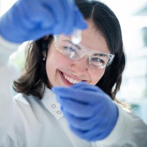 Smiling female scientist in lab inspecting a vial closely