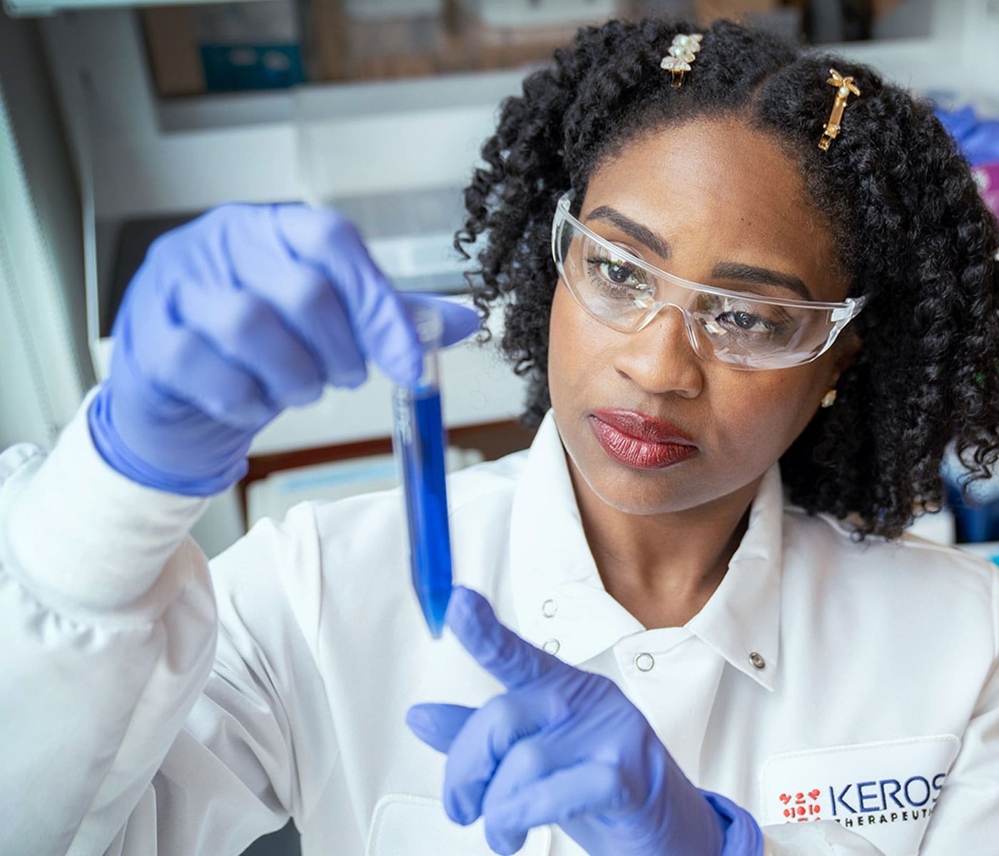 Female Keros Therapeutics scientist in a lab inspecting a vial of blue liquid